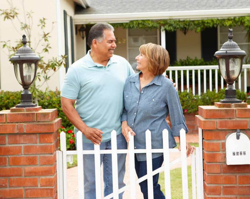 Older couple side hugging in front of house