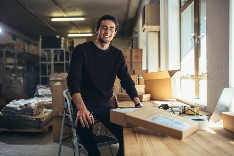 a smiling person sitting at a desk in a warehouse